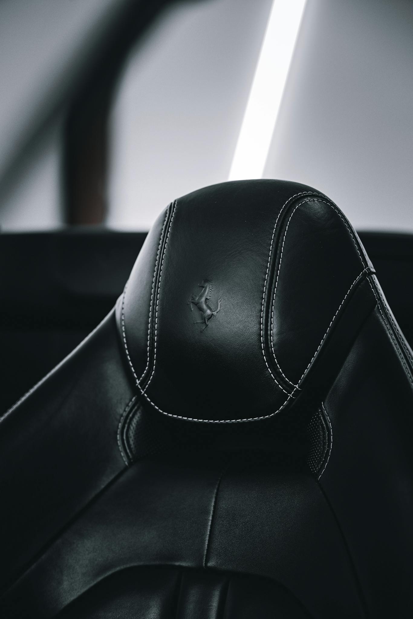 Close-up of a modern black leather car seat headrest with white stitching, offering a sense of luxury and comfort.